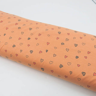 Jersey Stoff in Pfirsich mit kleinen Herz-Motiven in Rosa und Schwarz – elastischer Baumwolljersey für Kinder- und Damenkleidung, erhältlich bei Stoffrestposten.