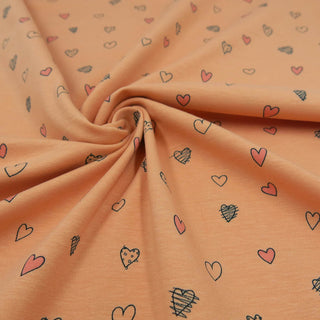 Jersey Stoff in Pfirsich mit kleinen Herz-Motiven in Rosa und Schwarz – elastischer Baumwolljersey für Kinder- und Damenkleidung, erhältlich bei Stoffrestposten.