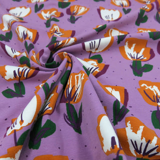 Fliederfarbener Jersey Stoff mit stilisierten Tulpen in Orange, Weiß und Grün – elastischer Baumwolljersey für Kleidung und Accessoires, verfügbar bei Stoffrestposten.